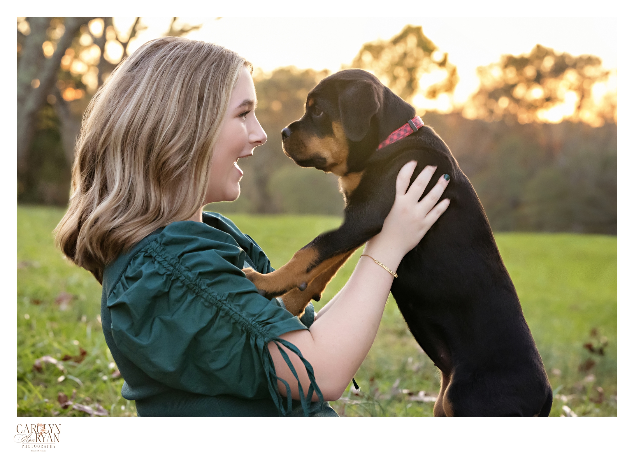 portrait of a high school senior holding her rottweiler puppy in the air. They are looking at each other